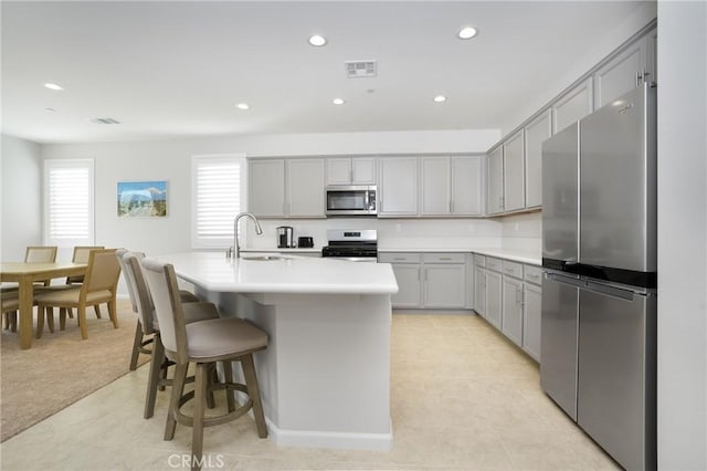 kitchen with light carpet, appliances with stainless steel finishes, sink, a center island with sink, and gray cabinets