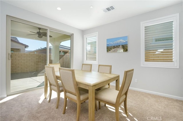 dining space with ceiling fan and light colored carpet