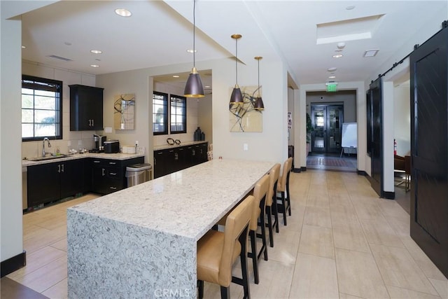 kitchen featuring light stone counters, a breakfast bar, sink, a barn door, and decorative light fixtures