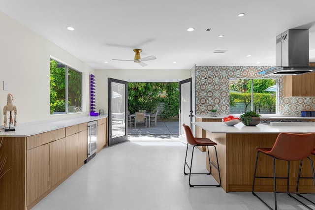 kitchen with wine cooler, ceiling fan, tasteful backsplash, island range hood, and a kitchen bar