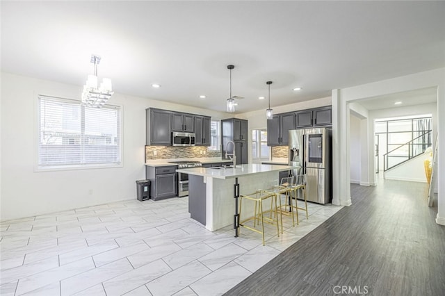 kitchen with a healthy amount of sunlight, a kitchen island with sink, hanging light fixtures, and appliances with stainless steel finishes