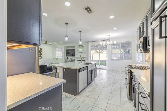 kitchen with a wealth of natural light, a center island with sink, ceiling fan with notable chandelier, and appliances with stainless steel finishes