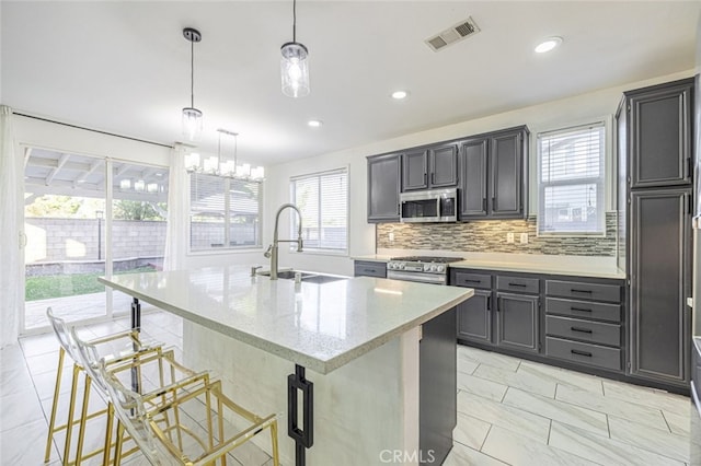 kitchen with decorative light fixtures, a kitchen bar, a kitchen island with sink, and appliances with stainless steel finishes