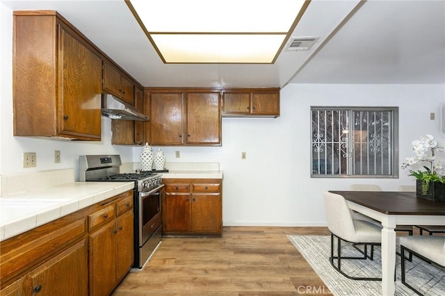 kitchen featuring gas range, light wood-type flooring, and tile countertops