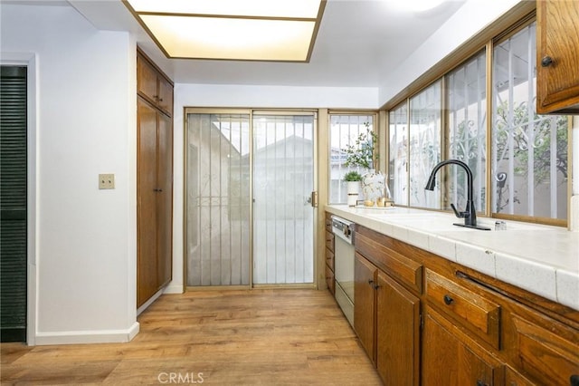 kitchen featuring tile countertops, light hardwood / wood-style floors, white dishwasher, and sink