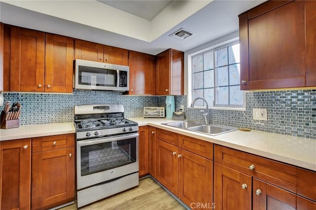 kitchen featuring decorative backsplash, appliances with stainless steel finishes, light wood-type flooring, and sink