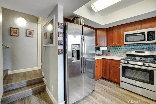 kitchen with light wood-type flooring, appliances with stainless steel finishes, and tasteful backsplash