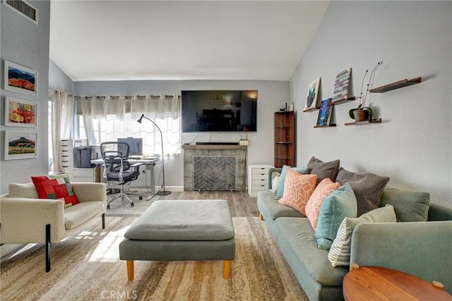 living room with light wood-type flooring, lofted ceiling, and a tiled fireplace