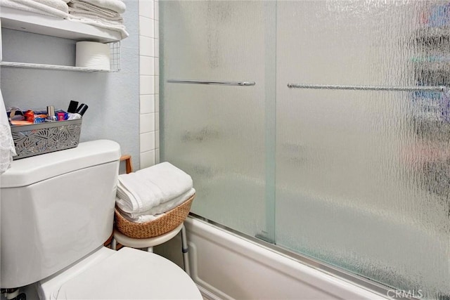 bathroom featuring toilet and bath / shower combo with glass door