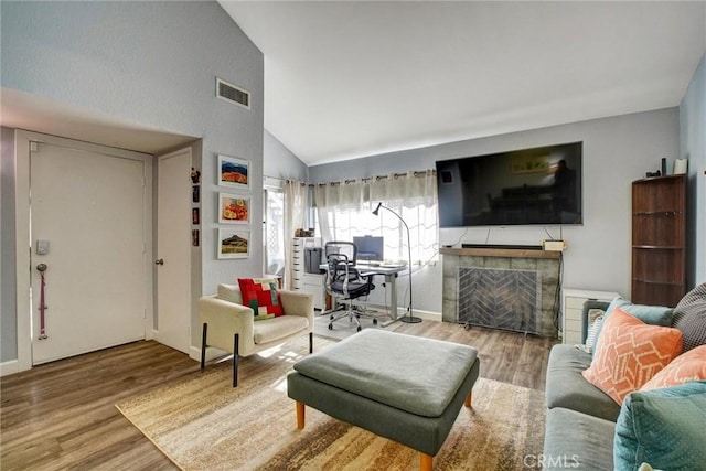 living room with hardwood / wood-style floors, lofted ceiling, and a tiled fireplace