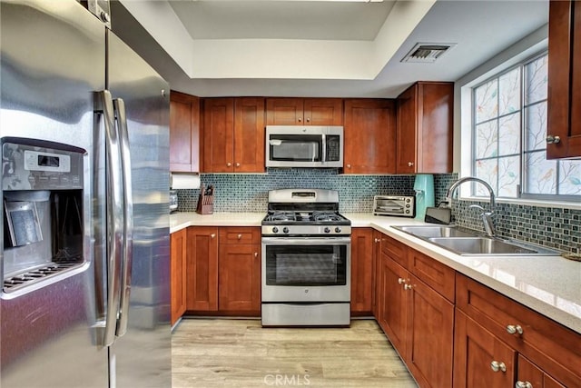 kitchen with backsplash, sink, light hardwood / wood-style floors, and appliances with stainless steel finishes