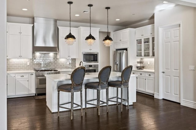 kitchen with high end appliances, wall chimney exhaust hood, and white cabinets