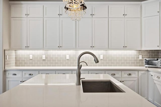 kitchen featuring sink, backsplash, white cabinets, and a notable chandelier