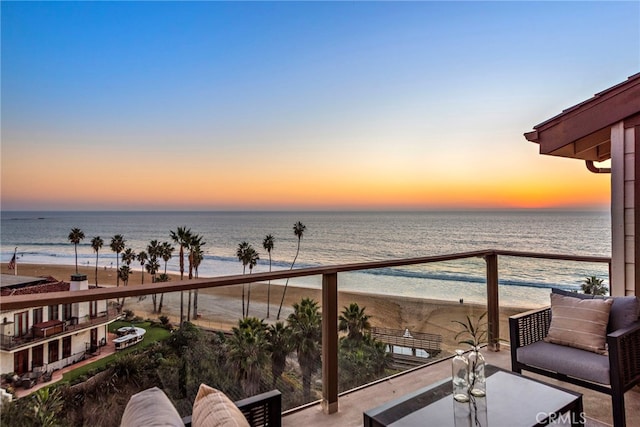 balcony at dusk with a water view and a view of the beach