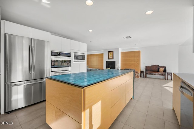 kitchen with white cabinets, appliances with stainless steel finishes, light tile patterned floors, and a kitchen island