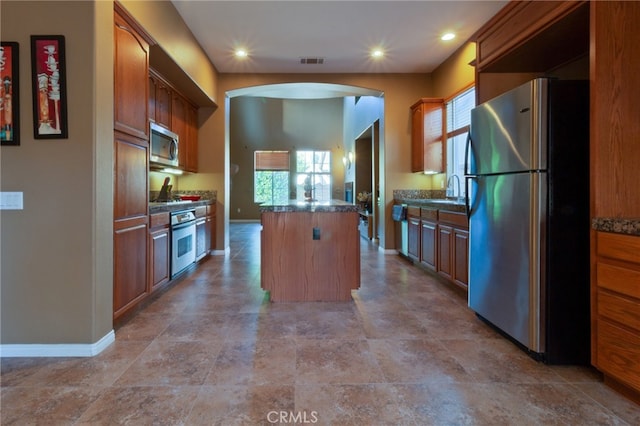 kitchen with stainless steel appliances, a kitchen island, dark stone countertops, and sink