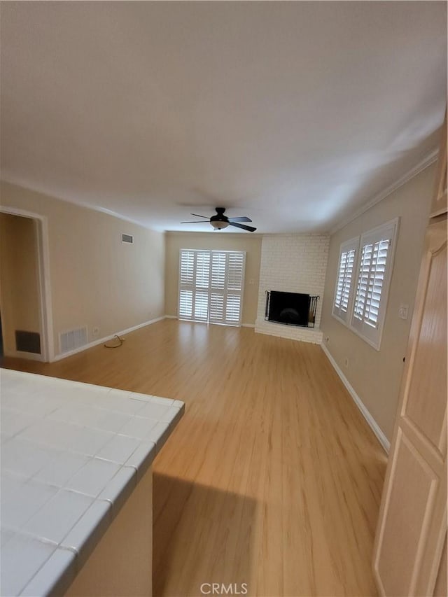 unfurnished living room with ceiling fan, a fireplace, crown molding, and light wood-type flooring