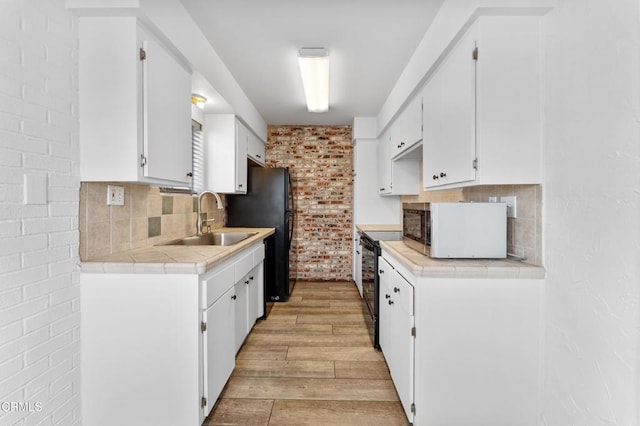 kitchen featuring brick wall, sink, black appliances, light hardwood / wood-style flooring, and white cabinets