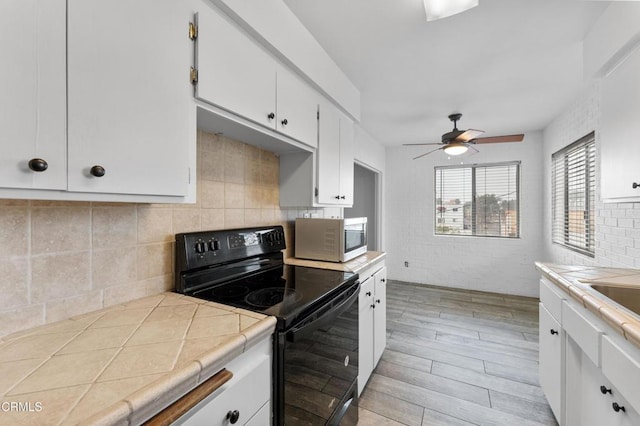 kitchen featuring tile countertops, ceiling fan, light wood-type flooring, black range with electric cooktop, and white cabinetry