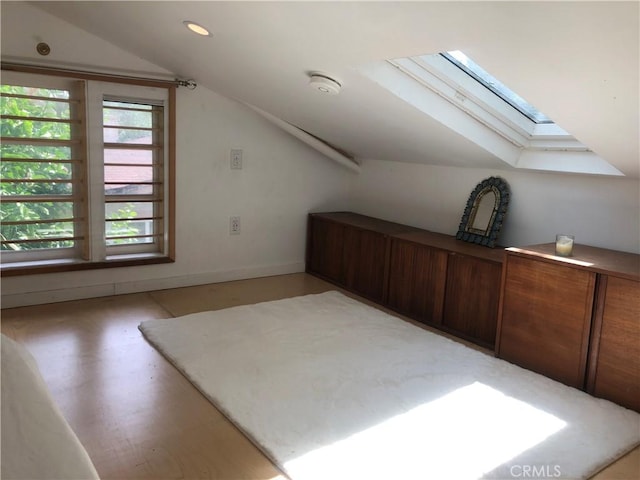 additional living space featuring lofted ceiling with skylight and light hardwood / wood-style flooring