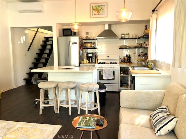 kitchen featuring pendant lighting, a kitchen breakfast bar, wall chimney exhaust hood, stainless steel appliances, and a wall unit AC