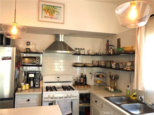 kitchen with white gas range, sink, wall chimney exhaust hood, tasteful backsplash, and stainless steel fridge