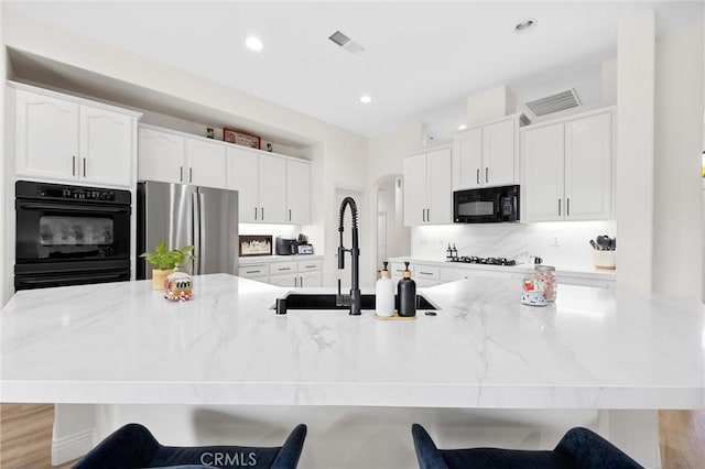 kitchen featuring white cabinetry, sink, a kitchen breakfast bar, light stone counters, and black appliances