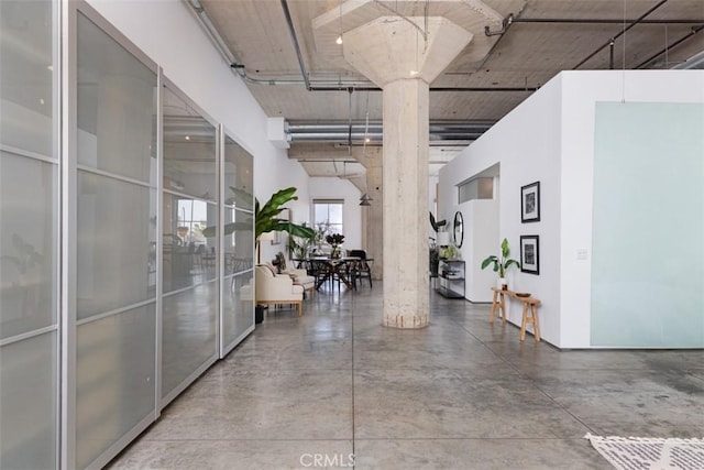 hall with concrete flooring, a high ceiling, and decorative columns