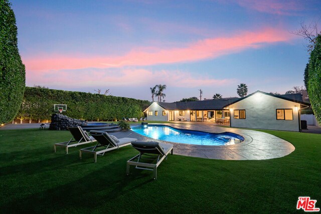 pool at dusk featuring a patio area and a lawn