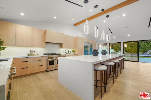 kitchen with lofted ceiling with beams, a spacious island, high quality appliances, light brown cabinetry, and light wood-type flooring