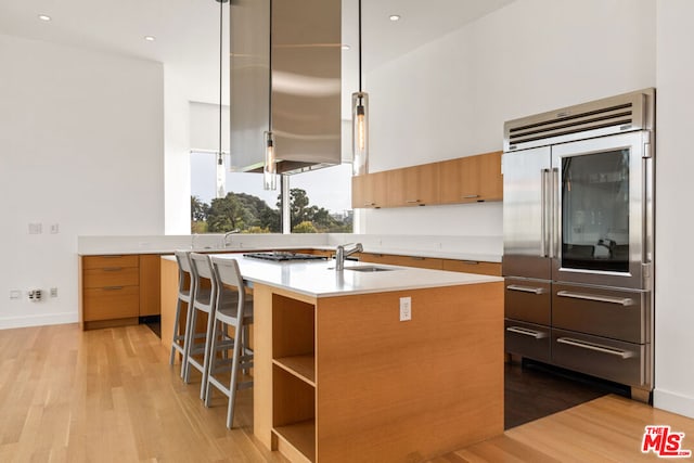 kitchen with sink, light hardwood / wood-style flooring, oven, a breakfast bar area, and an island with sink