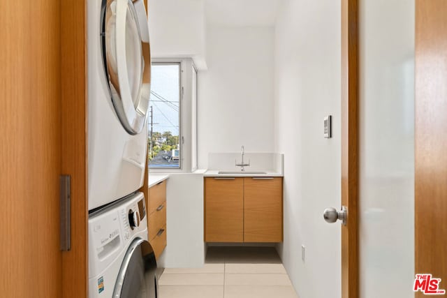 laundry area featuring light tile patterned flooring, cabinets, stacked washing maching and dryer, and sink