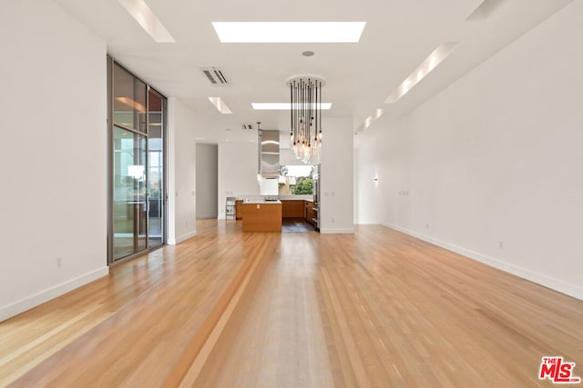 unfurnished living room with a notable chandelier, light hardwood / wood-style floors, a healthy amount of sunlight, and a skylight