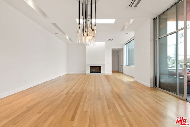 unfurnished living room with expansive windows, light hardwood / wood-style floors, an inviting chandelier, and a skylight