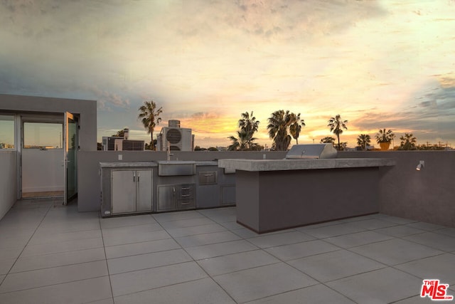 patio terrace at dusk featuring a grill, exterior kitchen, and sink