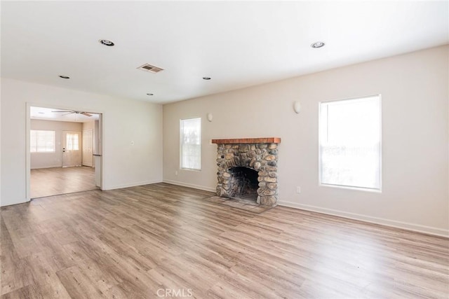 unfurnished living room with a stone fireplace, ceiling fan, and light hardwood / wood-style flooring