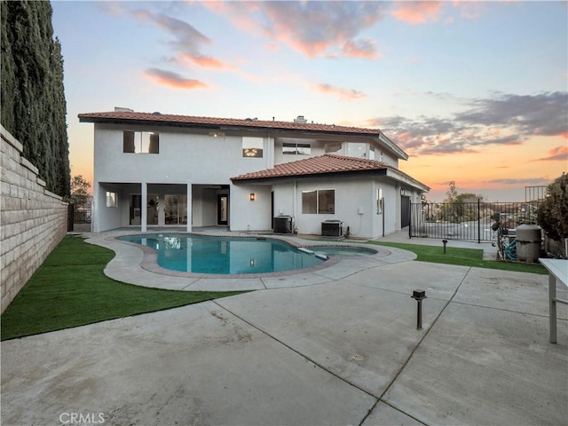 back house at dusk with central AC unit, a pool with hot tub, and a patio