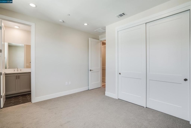 unfurnished bedroom featuring sink, connected bathroom, light colored carpet, and a closet