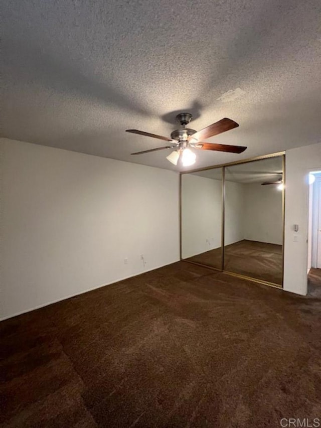 unfurnished bedroom featuring dark colored carpet, a textured ceiling, a closet, and ceiling fan