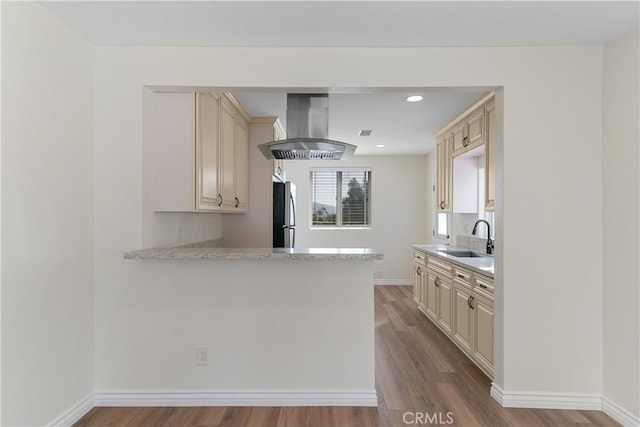 kitchen with light stone counters, sink, exhaust hood, cream cabinets, and light hardwood / wood-style flooring