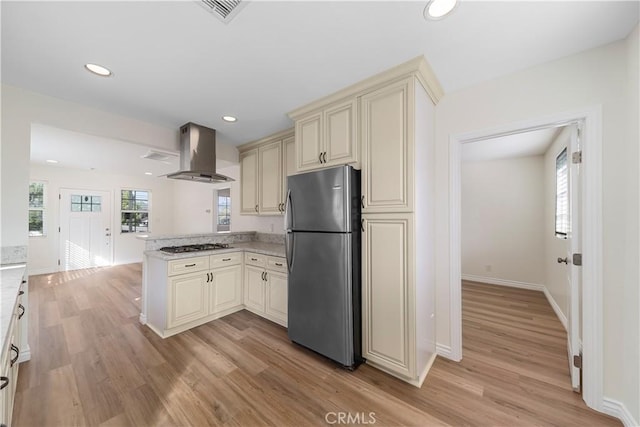 kitchen featuring wall chimney exhaust hood, light hardwood / wood-style flooring, stainless steel appliances, and cream cabinets