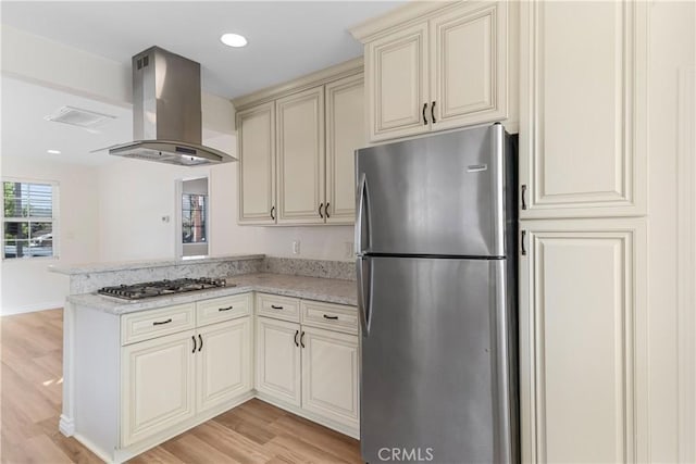 kitchen featuring light stone counters, light hardwood / wood-style flooring, island exhaust hood, cream cabinets, and appliances with stainless steel finishes