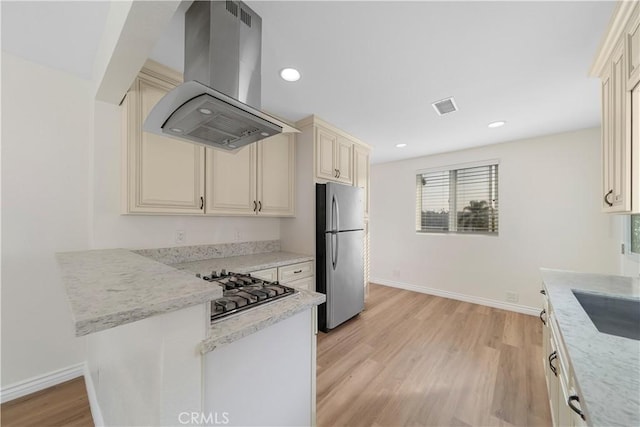 kitchen with stainless steel appliances, light stone counters, light hardwood / wood-style flooring, island exhaust hood, and cream cabinets