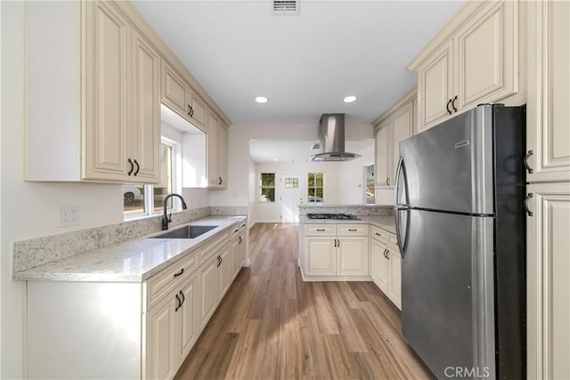 kitchen featuring sink, wall chimney exhaust hood, light hardwood / wood-style floors, kitchen peninsula, and stainless steel appliances