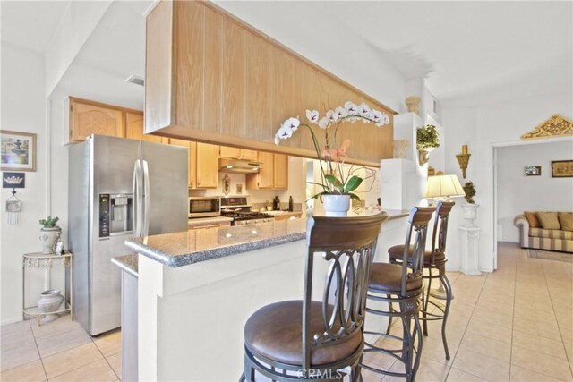 kitchen featuring kitchen peninsula, appliances with stainless steel finishes, light brown cabinetry, light stone counters, and light tile patterned floors