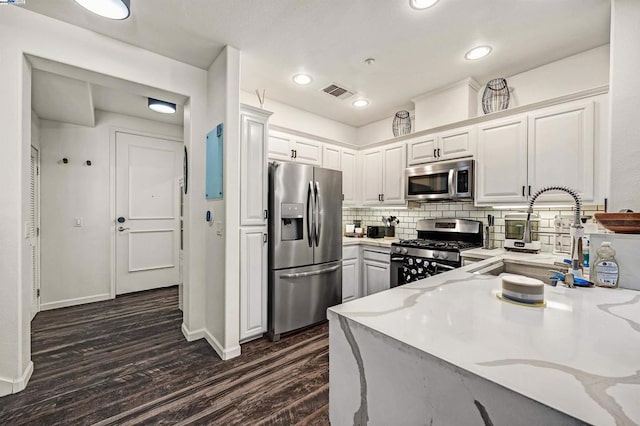 kitchen featuring stainless steel appliances, white cabinetry, dark hardwood / wood-style flooring, and backsplash