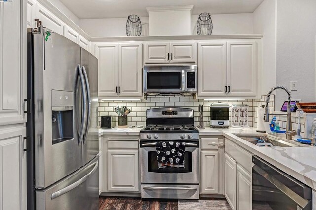 kitchen featuring stainless steel appliances, sink, white cabinetry, light stone counters, and decorative backsplash