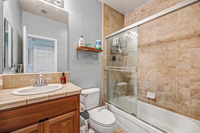 full bathroom with vanity, shower / bath combination with glass door, decorative backsplash, and toilet