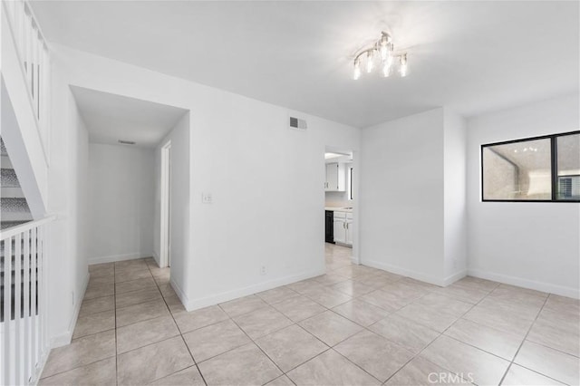 tiled spare room with an inviting chandelier