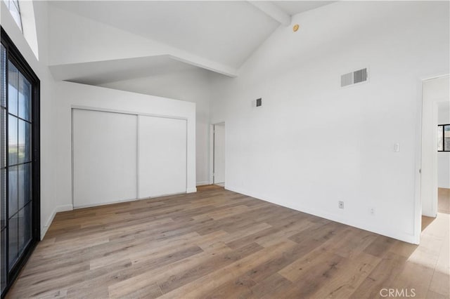 unfurnished bedroom with beamed ceiling, light wood-type flooring, high vaulted ceiling, and a closet